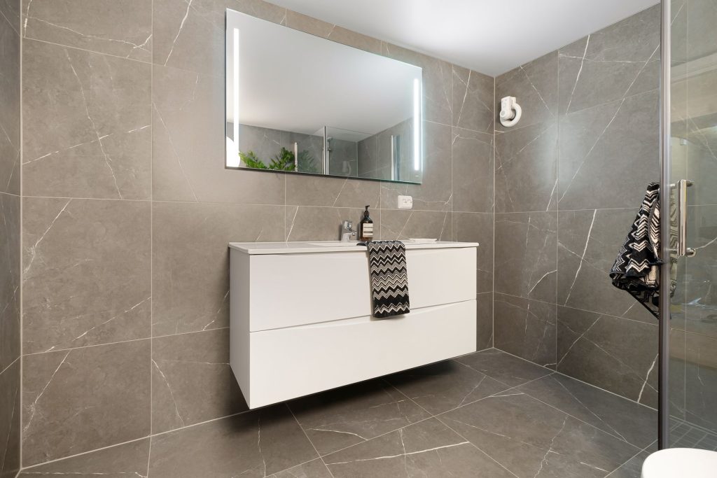 Modernes Bad mit großformatigen grauen Wandfliesen und bodenebener Dusche