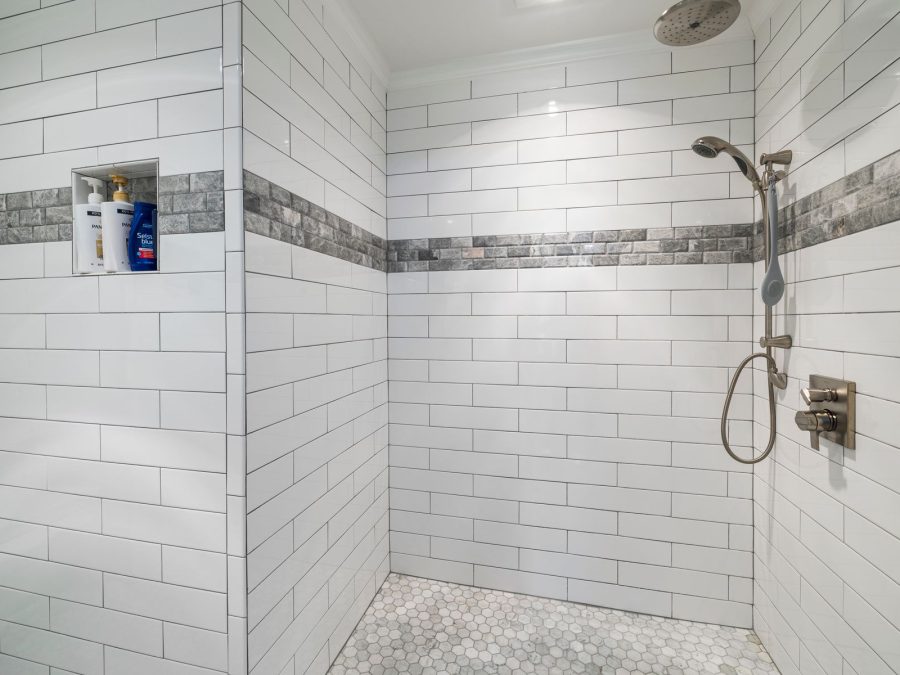 Geflieste bodenebene Dusche mit weißen Wandfliesen und Mosaikband